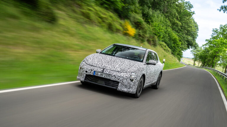The Kia EV4 drives at speed along a racetrack, with green grass blurring in the background