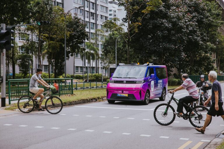An Ai.R AV – a WeRide GXR – on a test run in Punggol, Singapore. The vehicle is at an intersection with bicycles and pedestrians crossing the road in front of it
